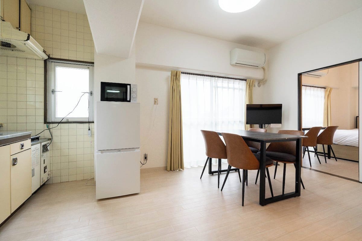A compact hotel room with a kitchenette, a dining area with a table and chairs, a TV, and a bed.