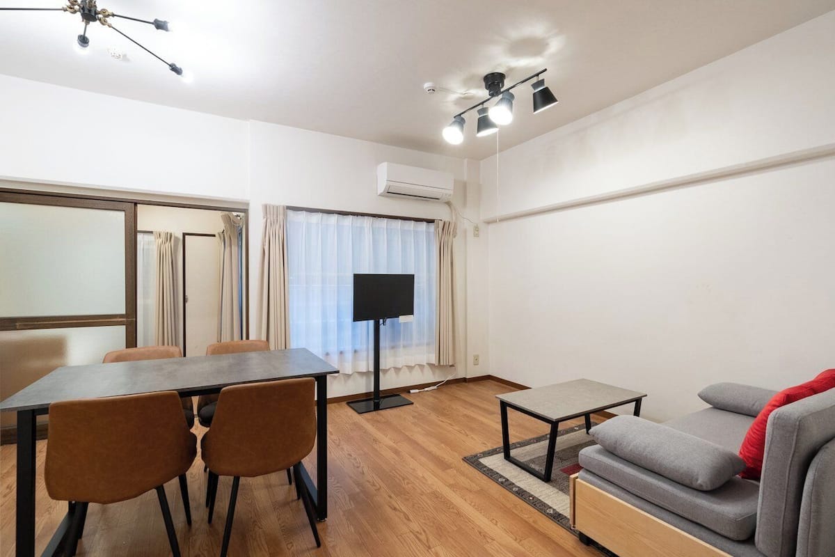 A room with a dining table, chairs, a TV, a sofa, and a ceiling fan.