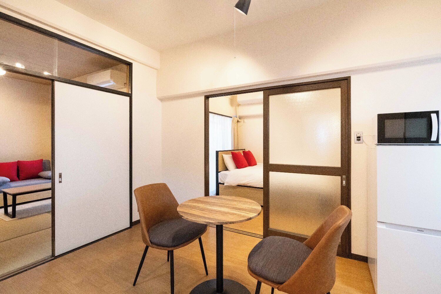 Habitación de hotel con cama, microondas, una pequeña mesa con dos sillas y puerta corrediza que da a otra habitación.