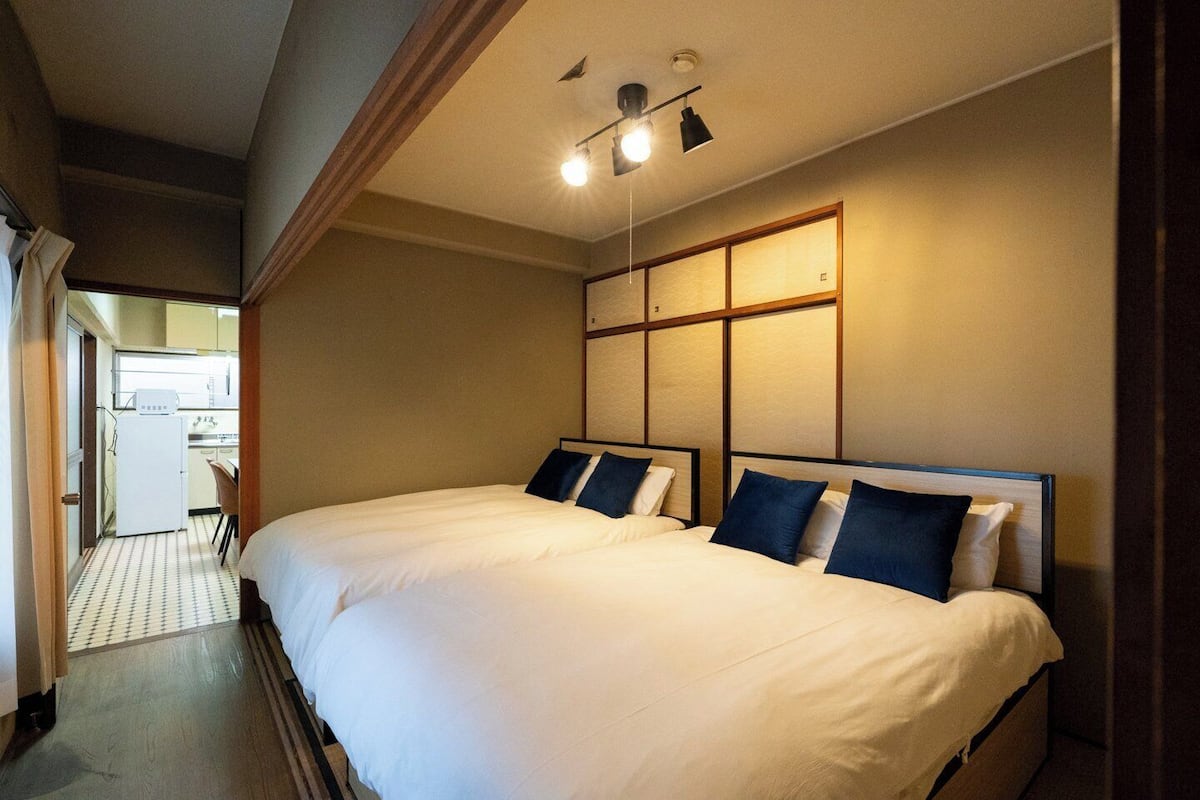 A hotel room with two beds, a kitchenette, and a bathroom.