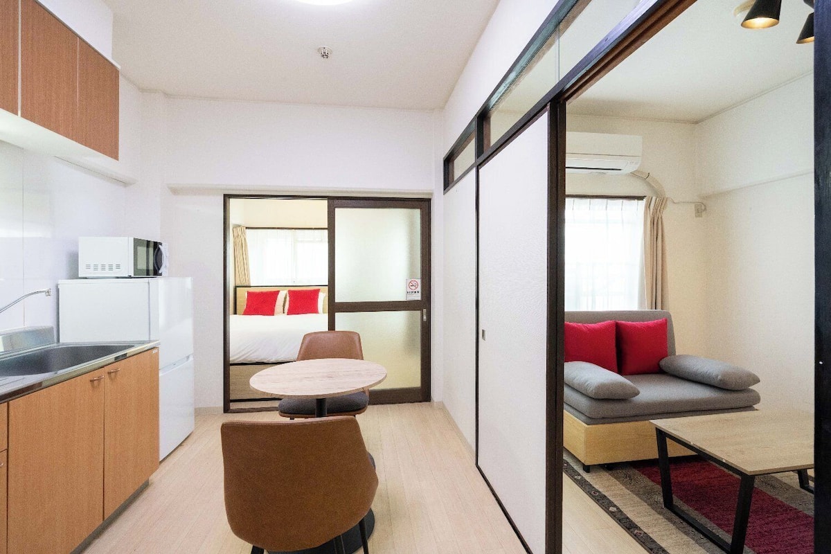 A compact hotel room with a kitchenette, a dining area, a sofa, and a bed.