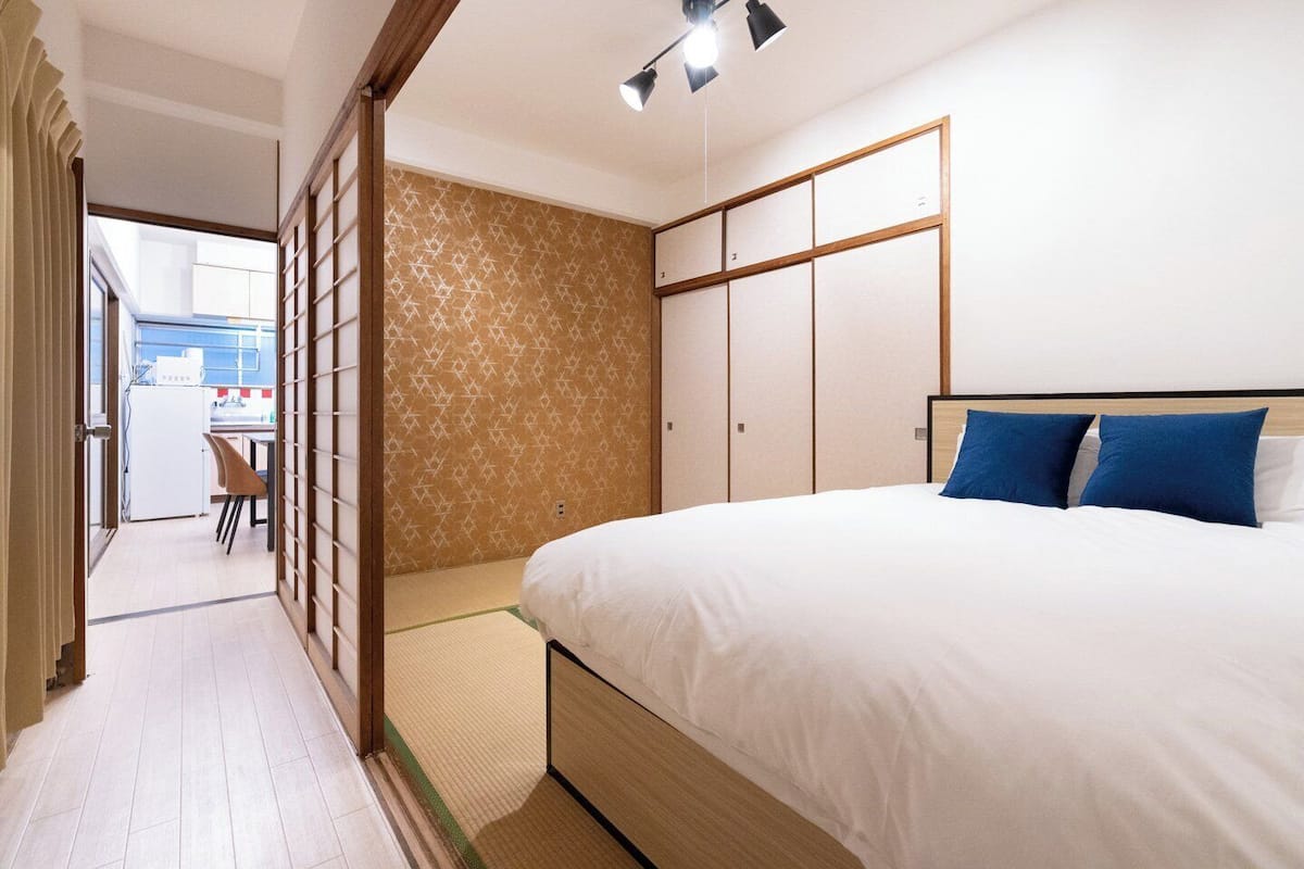 A bedroom with a bed, a wardrobe, and a view of a kitchen area.