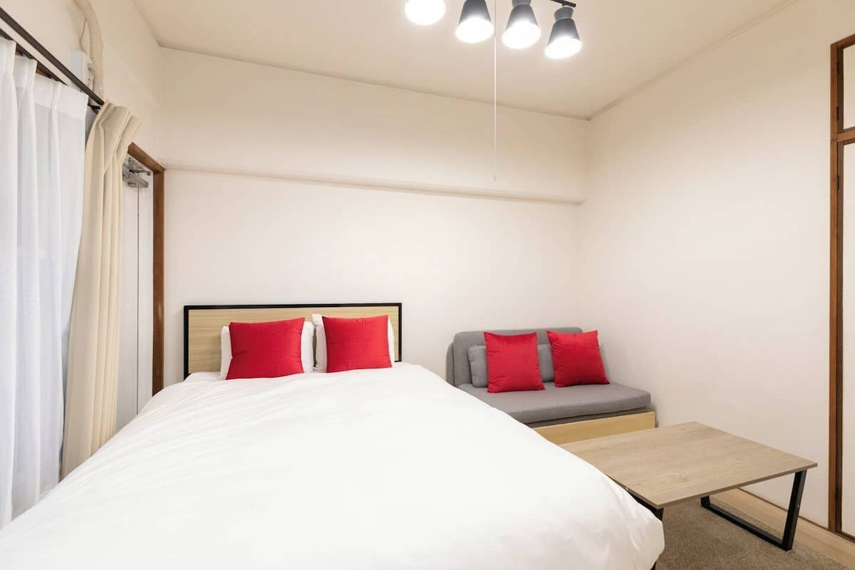 A hotel room with a bed, a sofa, a small table, and a ceiling light fixture.