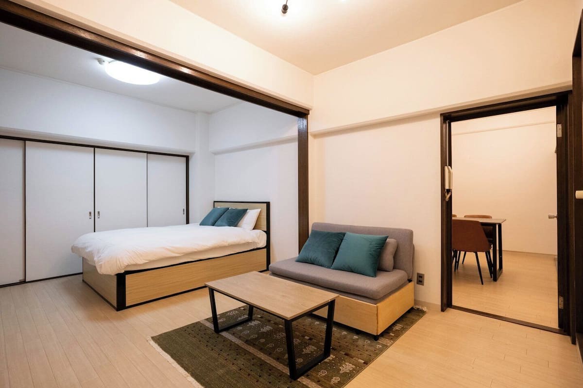 A compact room with a bed, a sofa, a small table, and a dining area.