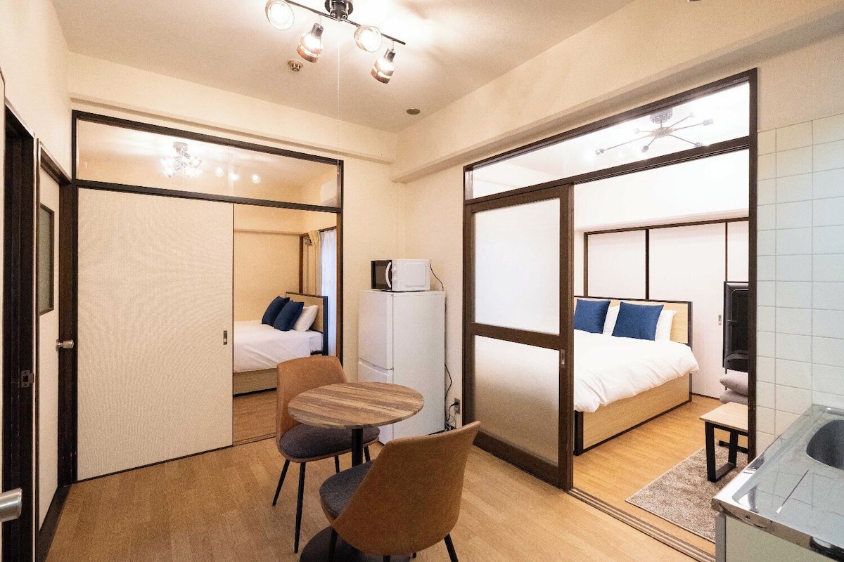 A compact hotel room with a bed, a small table, a chair, a microwave, and a TV.