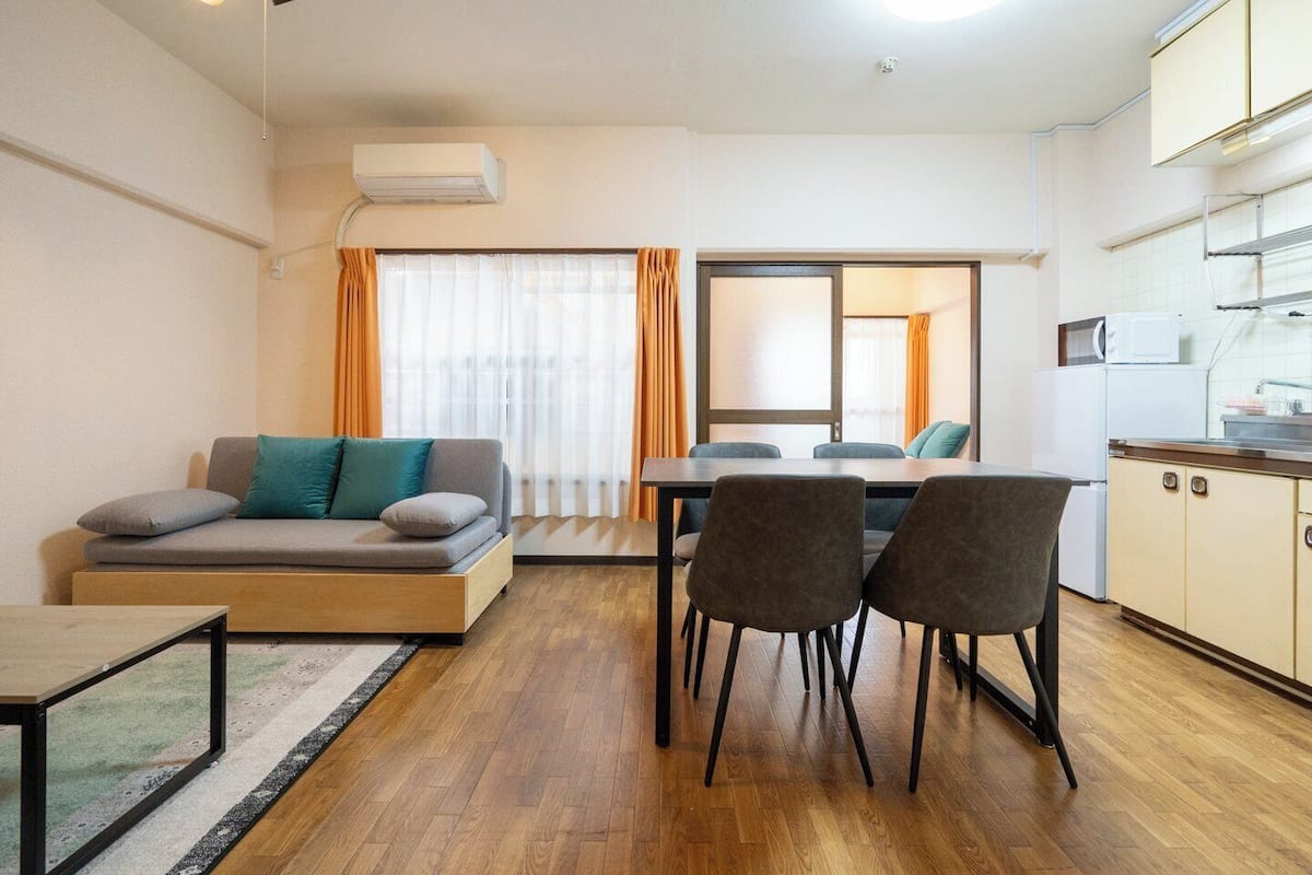 A modern living room with a sofa, chairs, a dining table, and a kitchen area with cabinets and a microwave.
