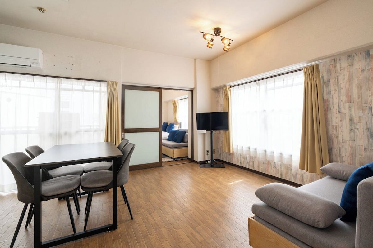 A hotel room with a dining table, sofa, TV, and large windows.