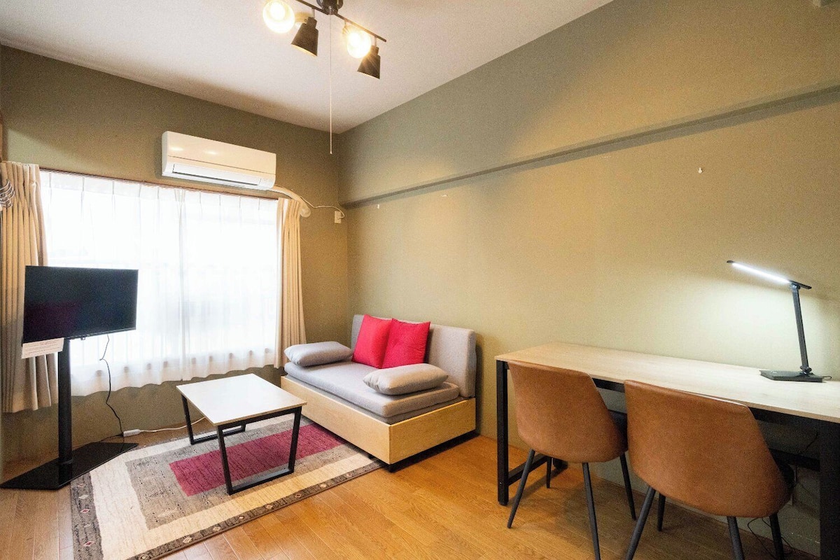 A room with a sofa, a desk, two chairs, a TV, and an air conditioning unit.