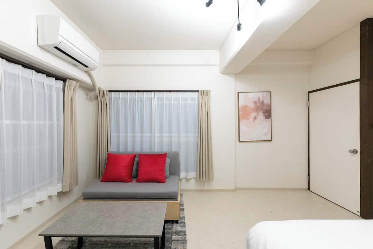 A modern room with a sofa, a table, a bed, an air conditioning unit, and a door.