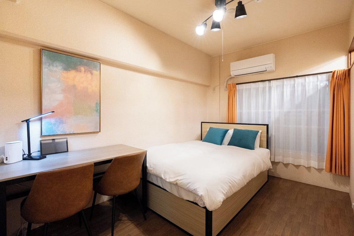 A hotel room with a bed, desk, chair, and an air conditioning unit.