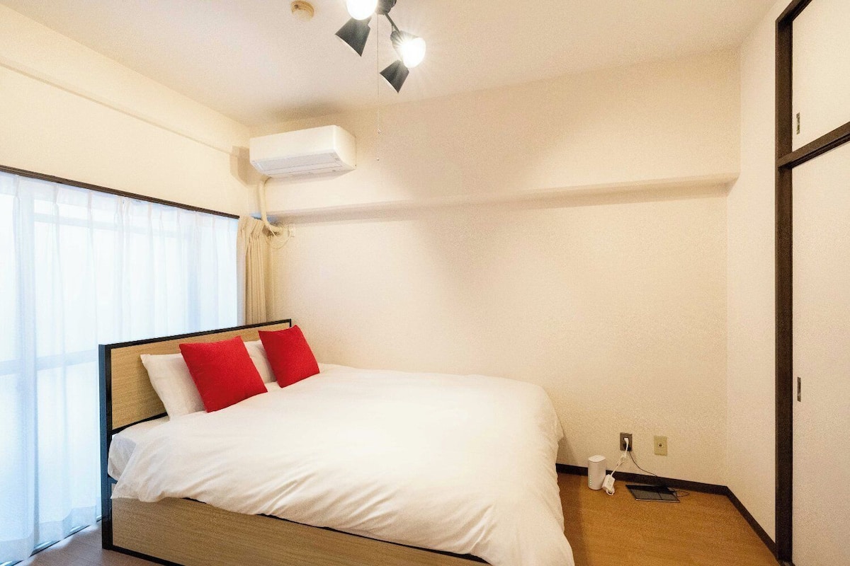A hotel room with a bed, a ceiling fan, an air conditioning unit, and a window with curtains.