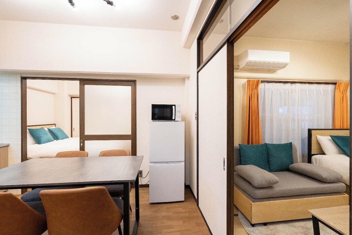A compact room with a bed, a dining table, a microwave, and a sofa.