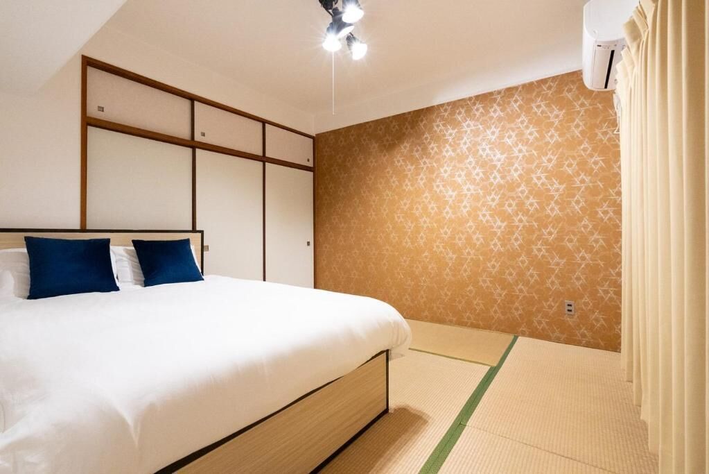 A hotel room with a bed, a wardrobe, a patterned wall, and a ceiling light fixture.