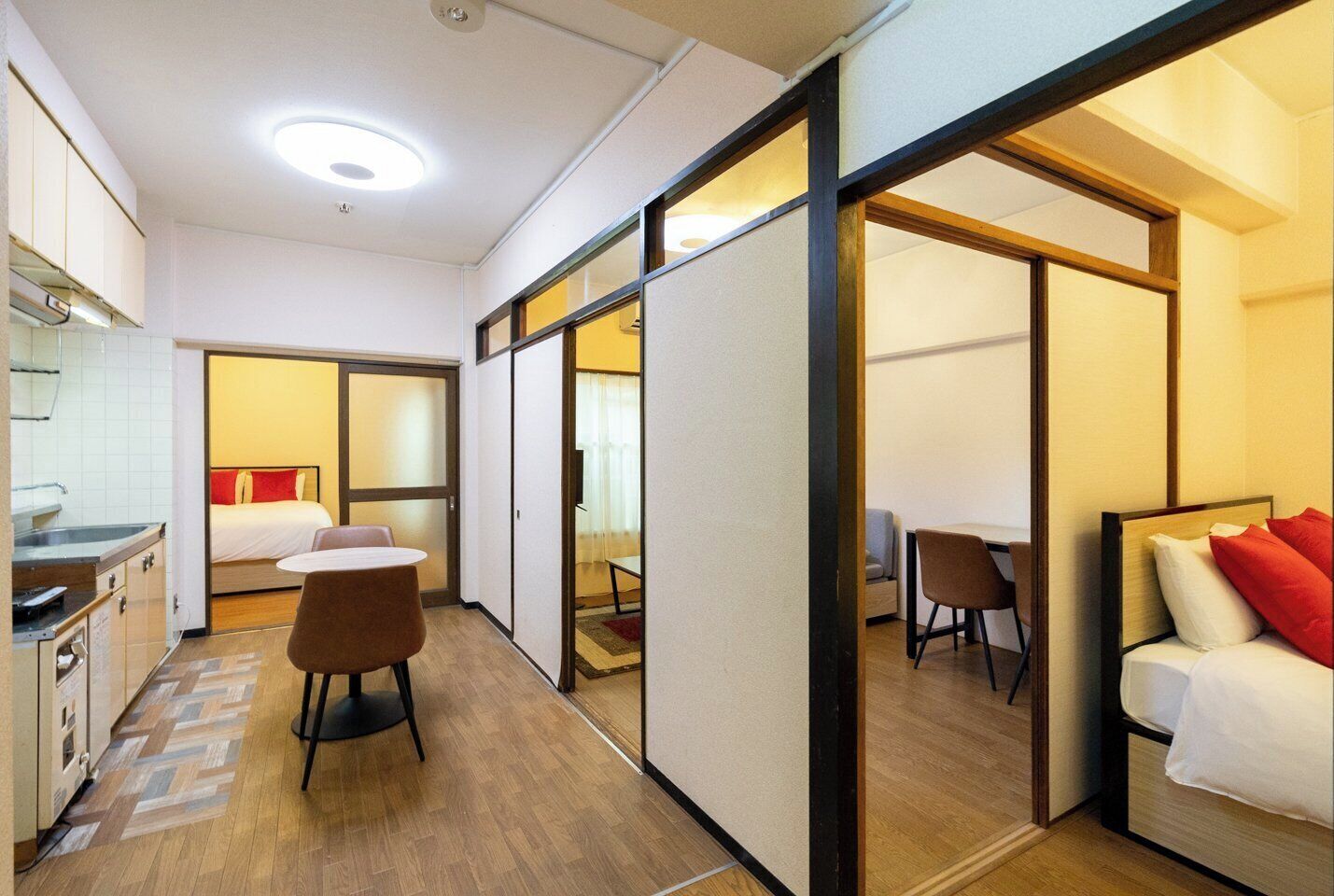 Una habitación de hotel con kitchenette, una cama con almohadas rojas, un escritorio y una silla.