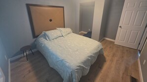 Une chambre à coucher avec un lit, une table de chevet, une porte et un luminaire au plafond.