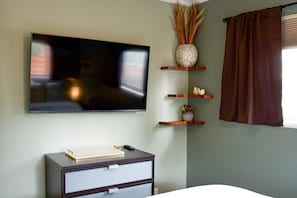 Ein Zimmer mit einem an der Wand montierten Flachbildfernseher, einer Holzkommode mit Schubladen und drei Holzböden mit Dekorationen.