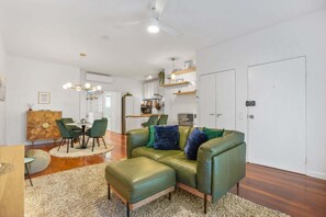 A modern living room with a green leather sofa, a dining area with a round table, and a kitchen in the background. - Peaceful 1-Bed Apartment Near Brisbane's Heart (Fortitude Valley)