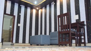 A room with a patterned wall, a wooden chair, a grey sofa, and a tiled floor. - Hotel Awadh Vilas (Ayodhya)
