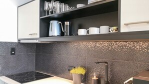 A modern kitchen with a black backsplash, stainless steel appliances, and a built-in shelf with glassware and cups. - Stylish Studio with Full Kitchen on Hobson Street (Auckland Central)
