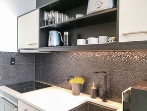 A modern kitchen with a black backsplash, stainless steel appliances, and a built-in shelf with glassware and cups. - Stylish Studio with Full Kitchen on Hobson Street (Auckland Central)