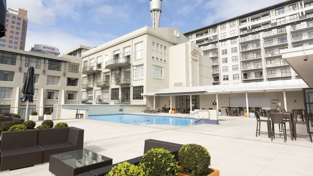 A rooftop pool area with lounge seating, a glass table, and a view of a tower. - Stylish Studio with Full Kitchen on Hobson Street (Auckland Central)