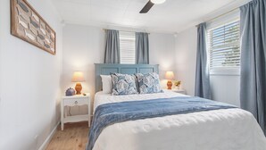 Une chambre à coucher avec un lit, des tables de chevet, un ventilateur de plafond et une fenêtre avec des rideaux.
