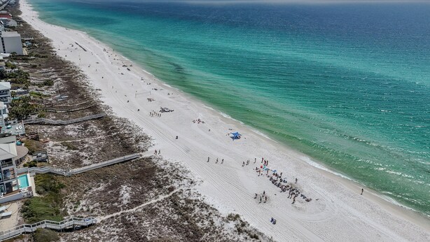 Une plage offrant une vue dégagée sur l’océan, un rivage sablonneux et un bâtiment doté d’une piscine.