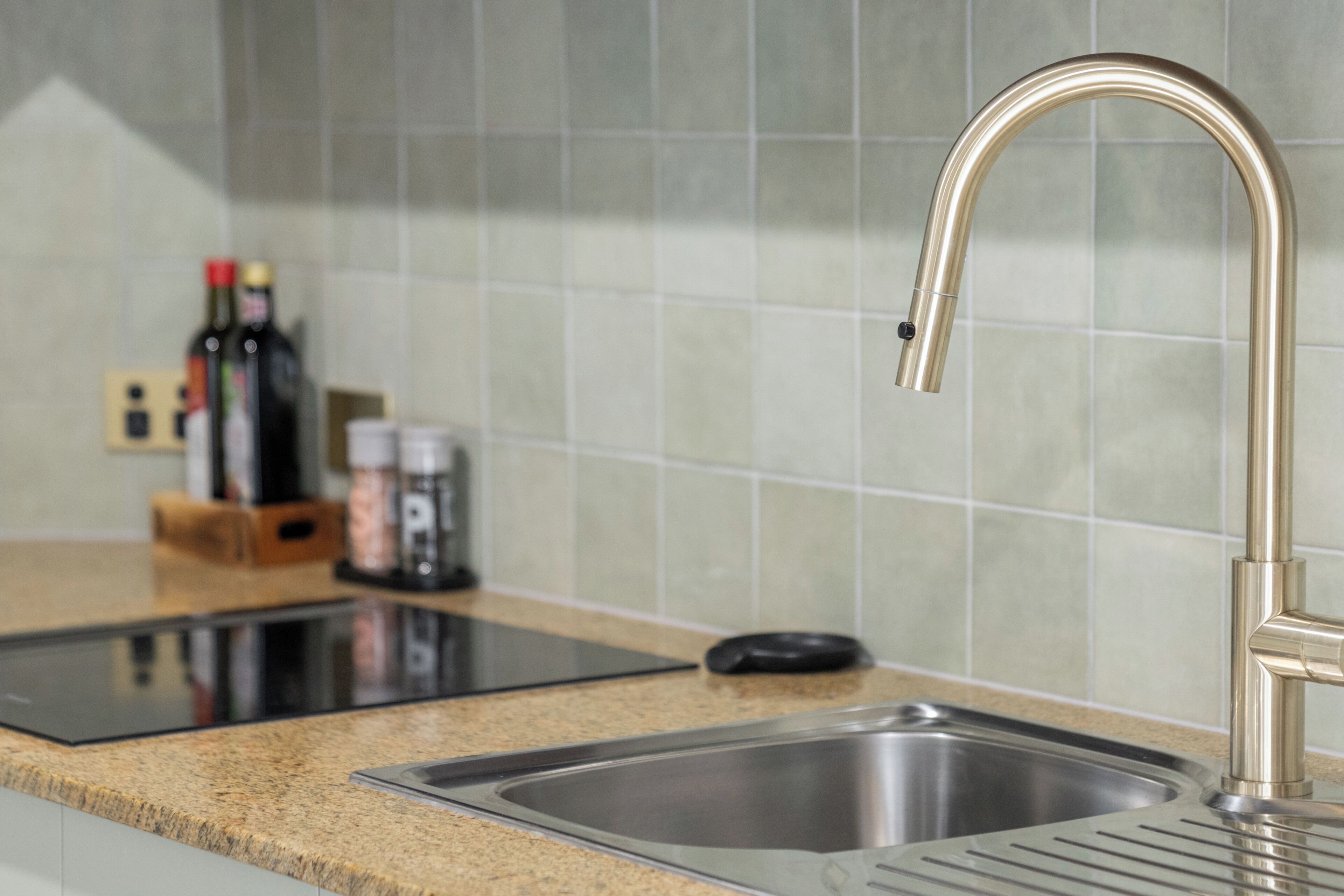 A kitchen with a stainless steel sink, a black induction cooktop, and a tiled backsplash.