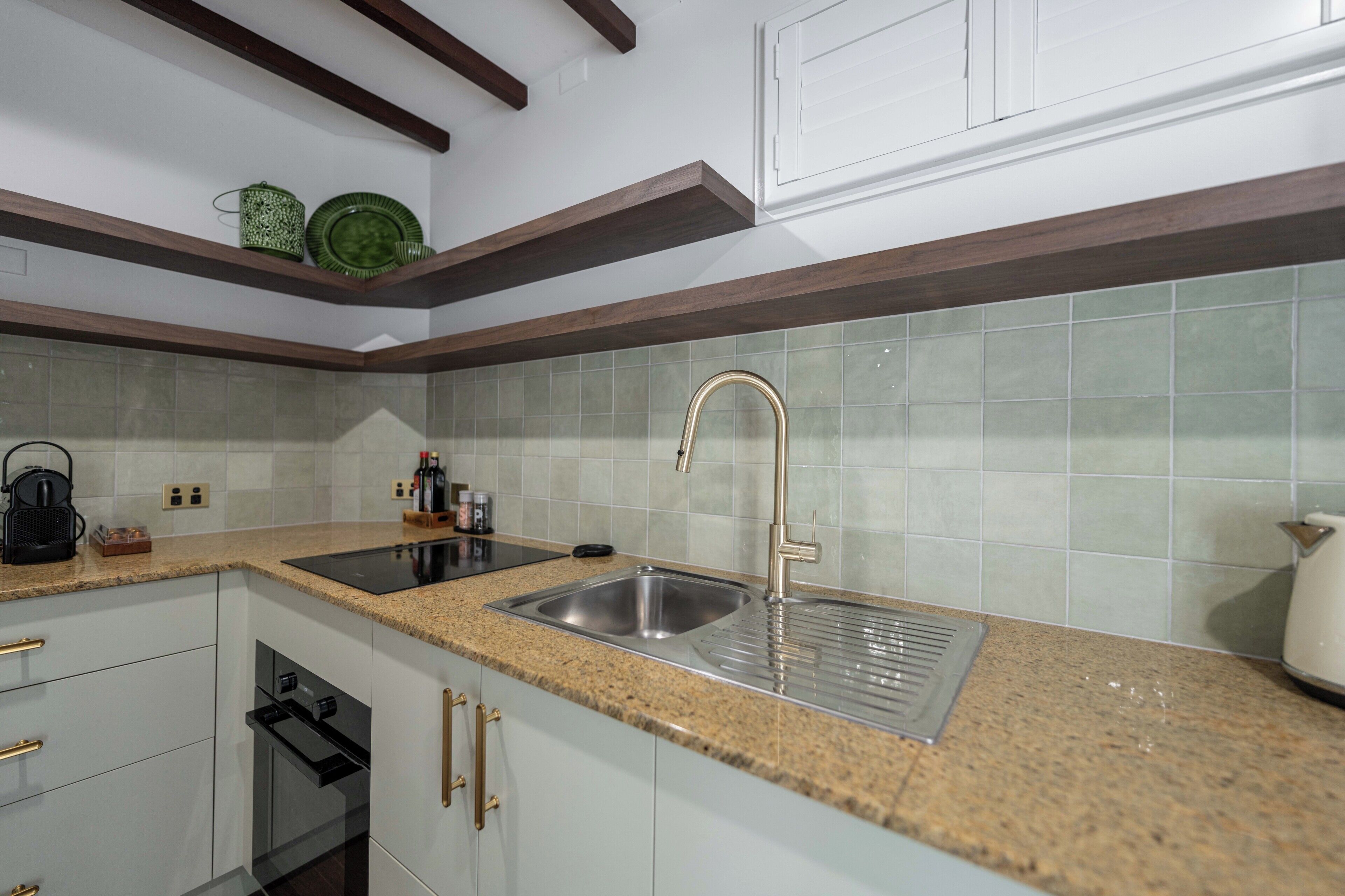 Una cocina con encimeras de granito, pileta de acero inoxidable, alacenas blancas y horno empotrado.