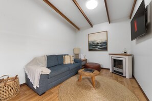 A living room with a sofa, a round coffee table, a fireplace, and a mounted TV. - Lakes Edge Retreat (Yungaburra)