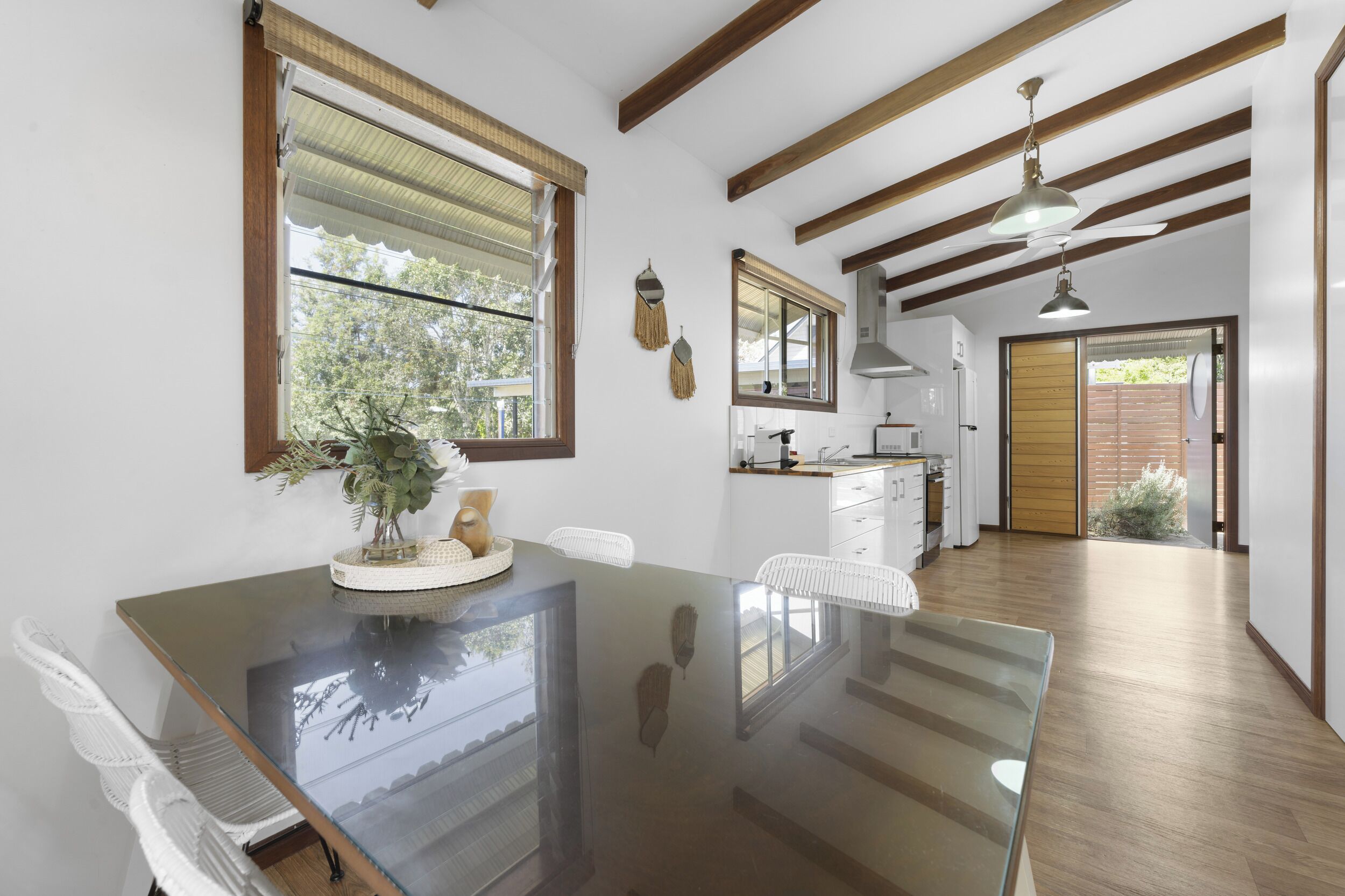 A modern kitchen with a glass dining table, wooden beams, and a view to the outside.