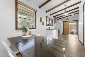 A modern kitchen with a glass dining table, wooden beams, and a view to the outside. - Lakes Edge Retreat (Yungaburra)