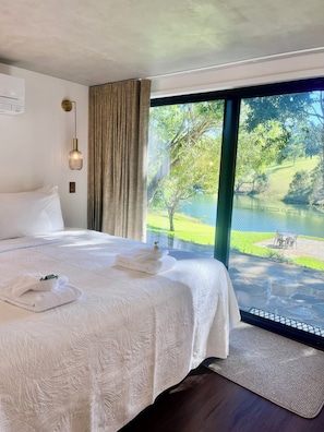 A hotel room with a large bed, a view of a lake, and a dining area outside.
