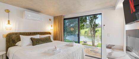 A modern hotel room with a large bed, a television, and a view of a lake.
