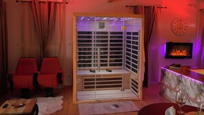 A room with a sauna, two red chairs, a fireplace, and a TV. - Luxury loveroom with private Jacuzzi, sauna, cinema corner & privacy area (Saint-Privat)