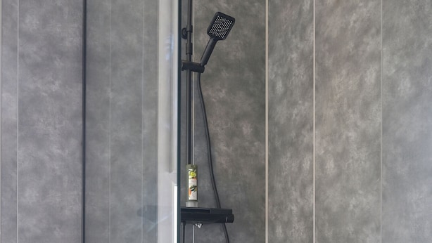 A modern shower with a handheld showerhead, a wall-mounted control panel, and a glass partition.