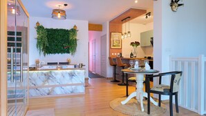 A modern kitchen with a marble island, a dining area with a round table, and a living space with a large plant wall. - Luxury loveroom with private Jacuzzi, sauna, cinema corner & privacy area (Saint-Privat)
