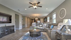 A spacious living room with a large flat-screen TV, a ceiling fan, a fireplace, and a dining area with a kitchen in the background. - Close to Disney! Home w/ Patio & Community Perks (Davenport)