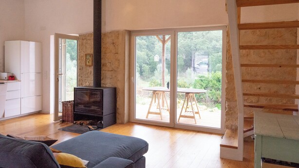 A living room with a fireplace, a sofa, a dining table, and a staircase. - Quiet, stylishly renovated. Fantastic view of fruit trees and cork oaks. (Tomar)