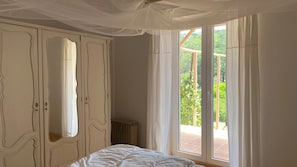 Une chambre à coucher avec un lit, une armoire et une grande fenêtre avec des rideaux.
