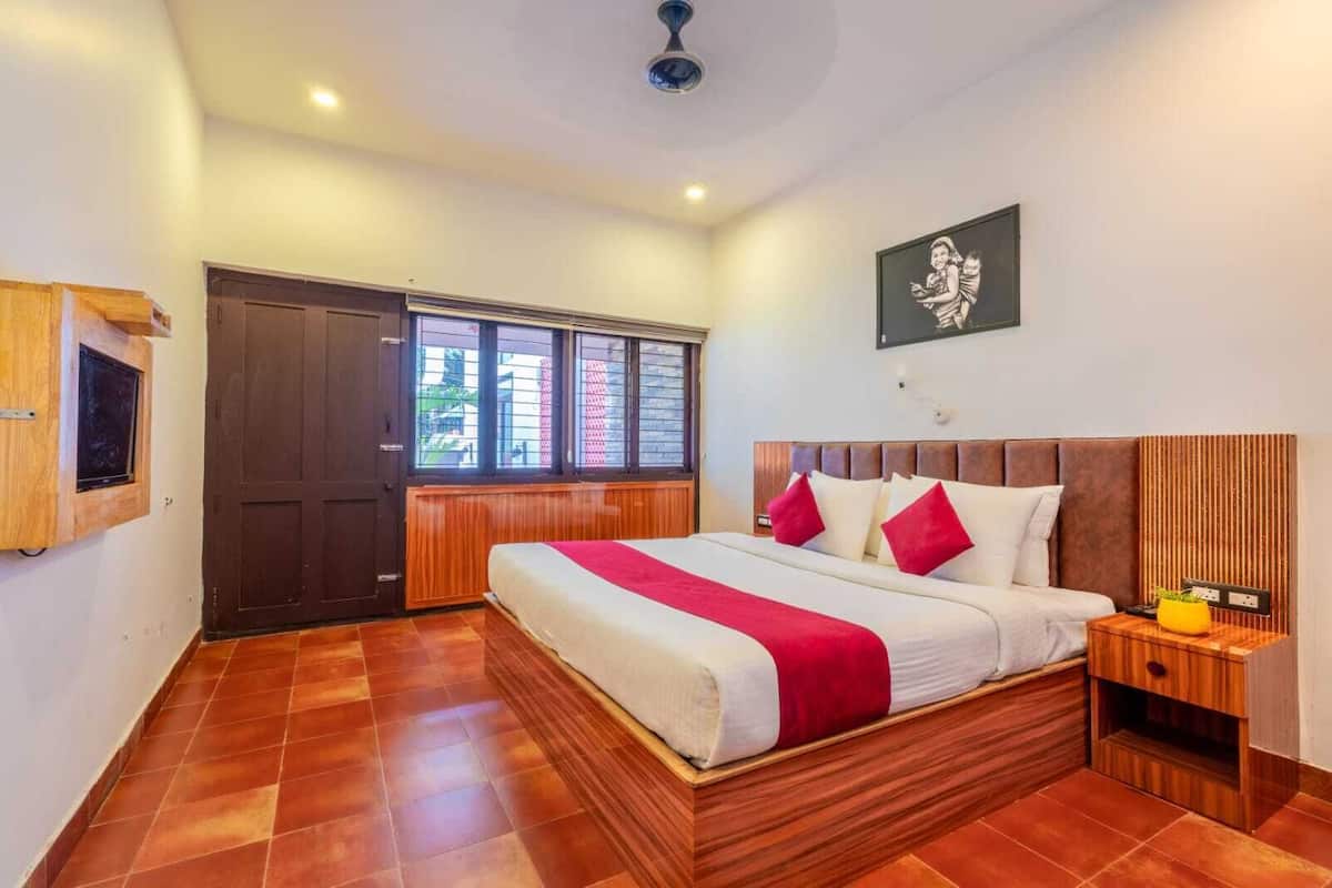 A bedroom with a wooden bed, a nightstand, a window with blinds, and a door.