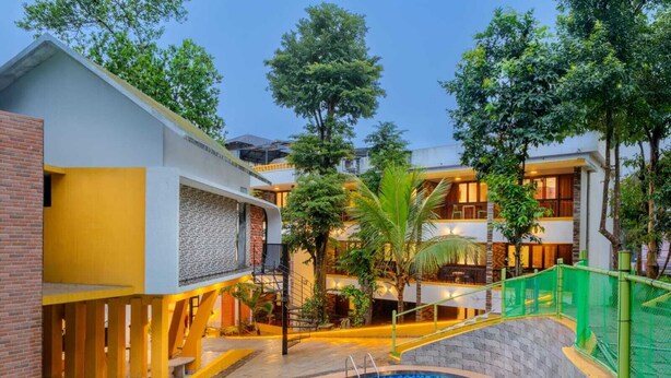 A hotel with a swimming pool, outdoor seating, and a multi-story building with balconies. - Karar Gardens (Kumily)