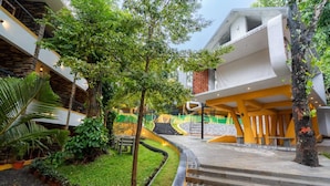 A modern building with a staircase leading to a covered area, surrounded by greenery and a small garden. - Karar Gardens (Kumily)