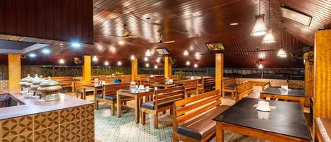 Un restaurante con mesas y bancos de madera, suelo estampado y techo inclinado con luces colgantes.