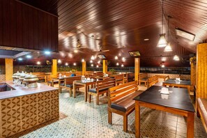 A restaurant with wooden tables and benches, a patterned floor, and a sloped ceiling with hanging lights. - Karar Gardens (Kumily)