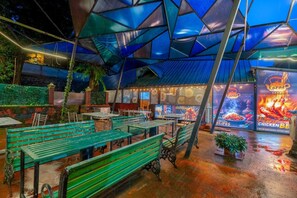 An outdoor dining area with green benches and a covered seating area with a blue roof. - Karar Gardens (Kumily)