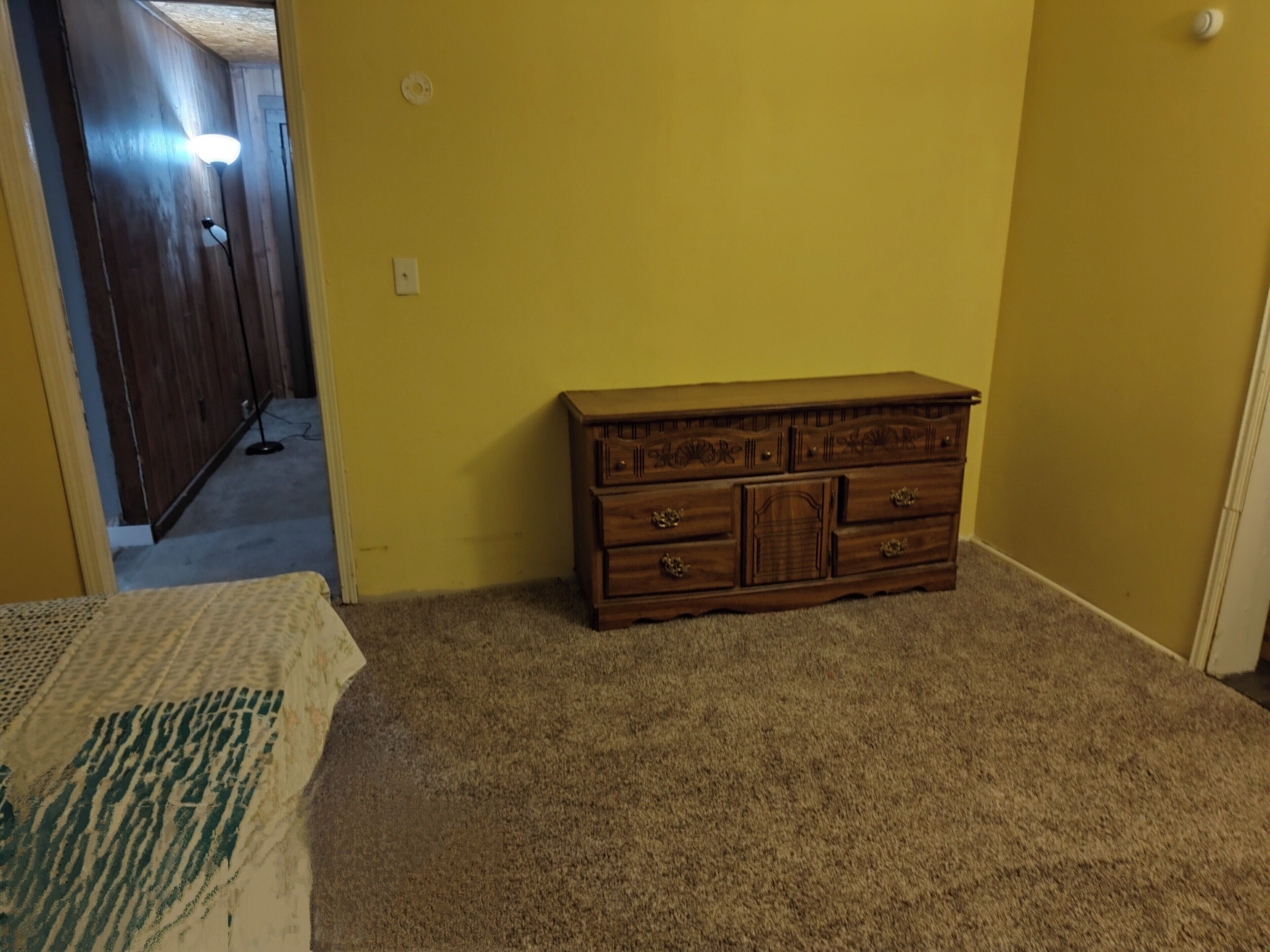 A room with a wooden dresser, carpeted floor, and a doorway leading to another room.