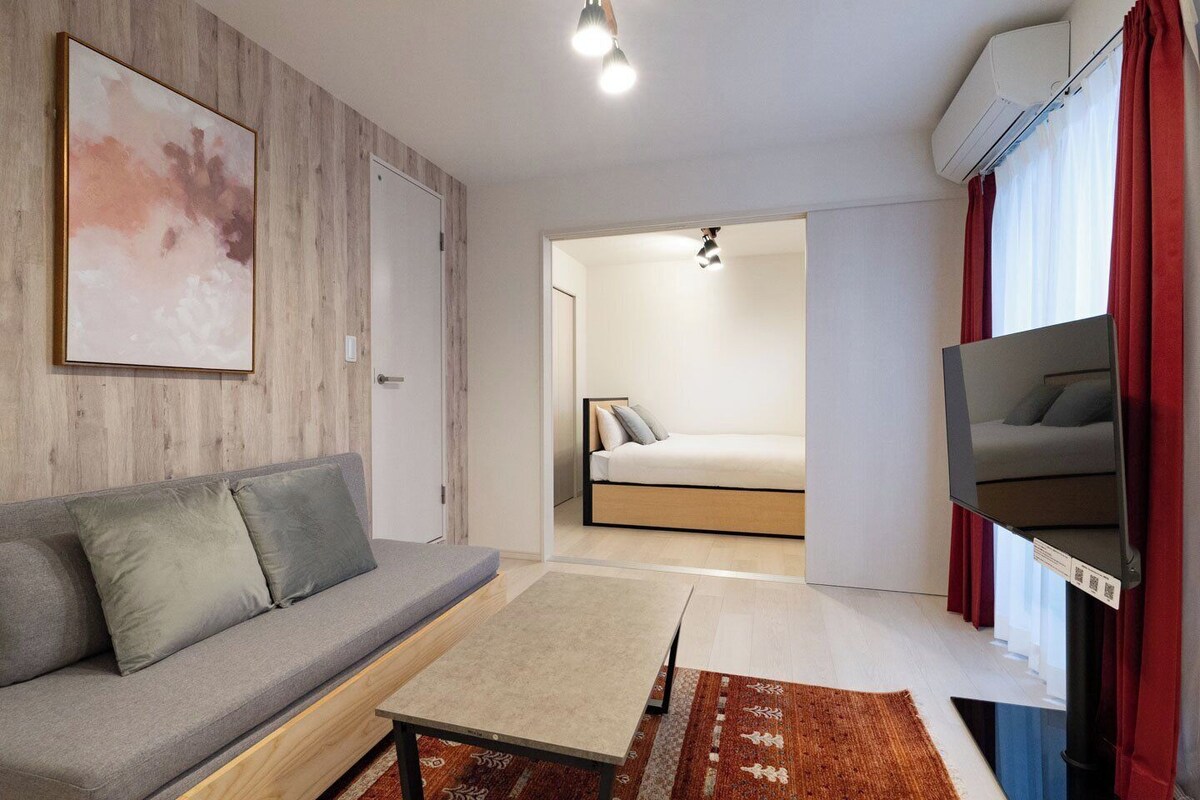Uma sala de estar moderna com sofá, televisão de tela plana, mesa de centro e uma cama ao fundo.