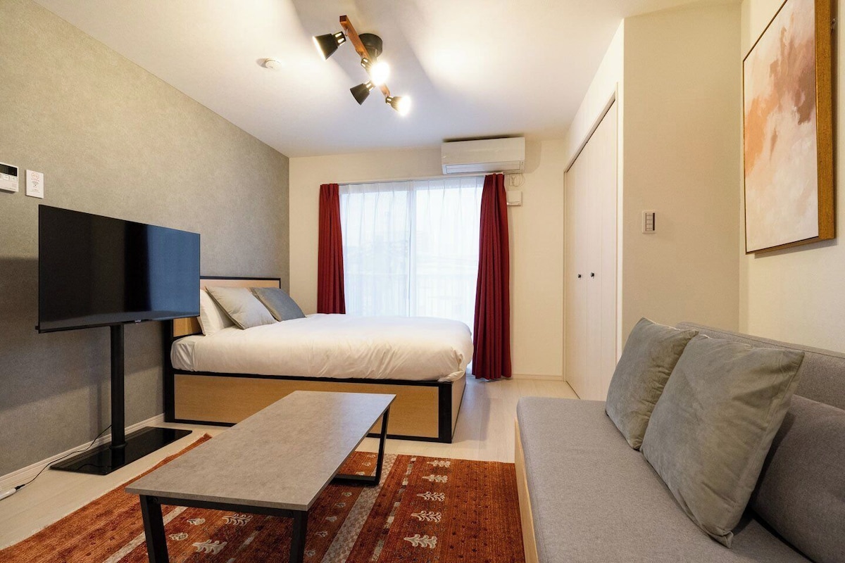 Quarto de hotel moderno com cama, sofá, televisão e ventoinha no teto.