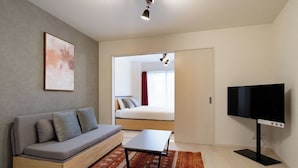 Quarto moderno com sofá, televisão, cama e vista para outro ambiente.